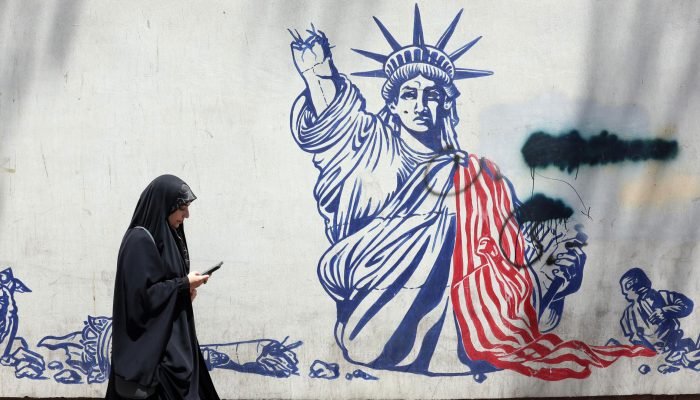 Mulher passa em frente a um mural anti-EUA em Teerã, capital do Irã. (Foto: EFE/ABEDIN TAHERKEN...
